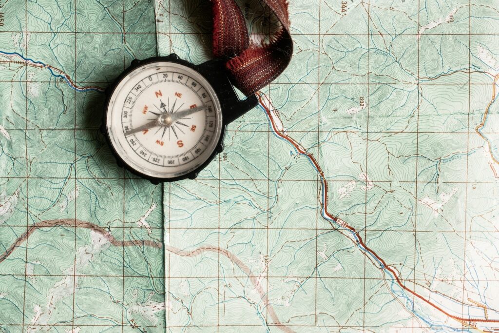 A magnetic compass with a woven strap resting on a detailed green topographic map with contour lines and roads.