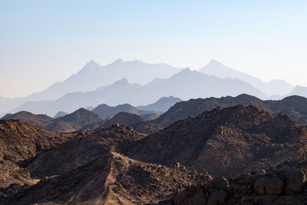 Layered desert mountain ranges receding into haze, with rocky terrain in the foreground and misty peaks in the distance.