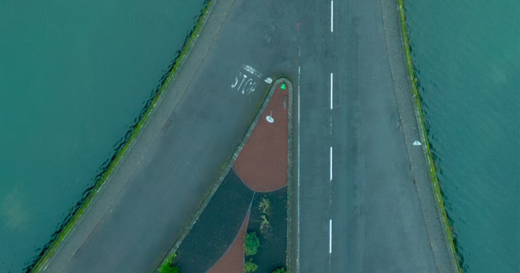 Two roads merging into one lane over turquoise water, viewed from above, symbolizing a corporate merger.