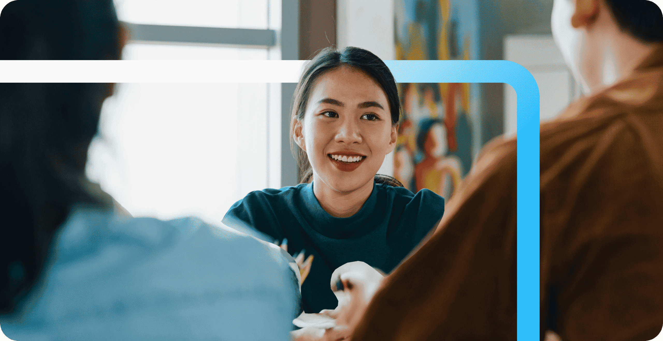 A smiling young woman in a teal shirt engages in conversation with colleagues at a Randstad center.