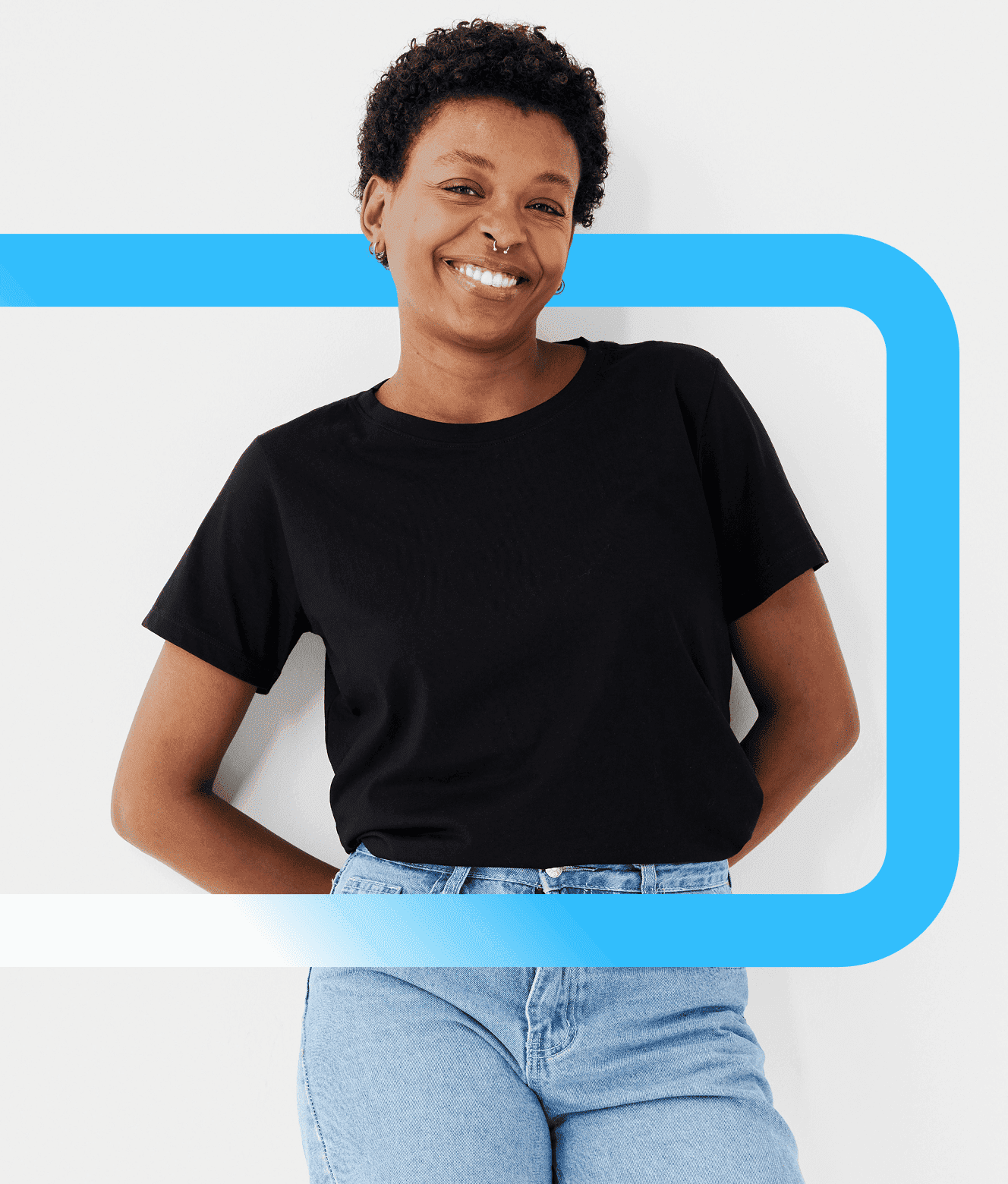 A smiling woman with short curly hair wearing a black t-shirt and blue jeans poses against a light background with a blue